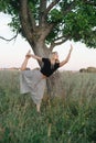 Balancing on one foot young blond woman exercising under a tree on grass