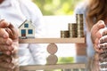 Balancing Of Stacked Coins And House Model On Seesaw Royalty Free Stock Photo