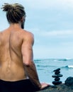 Balancing stones arranged in a pyramid shape with a back of a shirtless man meditating Royalty Free Stock Photo