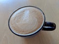 Balck cup of Cappuccino on saucer with a leaf pattern in foam Royalty Free Stock Photo