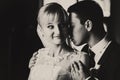 A balck and white picture of smiling bride and groom holding her