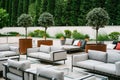 Balcony with white sofas and glass tables, surrounded with green trees and flowerpots.