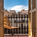 Balcony with a wrought iron railing, wooden sashes and wicker chair. Sunny day with blue sky. Barcelona, Spain. Royalty Free Stock Photo