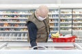 A bald adult man in a medical mask and gloves chooses frozen foods in a supermarket. Self-isolation and precautions during the