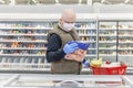 A bald adult man in a medical mask and gloves chooses frozen foods in a supermarket. Self-isolation and precautions during the