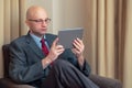 Bald attractive manager businessmen sitting on a chair in his hotel room looking at tablet. Royalty Free Stock Photo