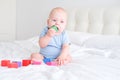 bald baby boy 3 months in blue bodysuit playing with children wooden cubes toys on bed Royalty Free Stock Photo