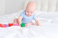 bald baby boy 3 months in blue bodysuit playing with children wooden cubes toys on bed Royalty Free Stock Photo