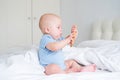 bald baby boy 3 months in blue bodysuit playing with wooden teether for teeth on bed Royalty Free Stock Photo