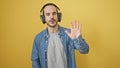 Bald bearded man in headphones waving against a yellow background