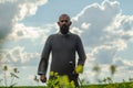 Bald bearded man in metal chain mail over linen shirt stands in the middle of field, holding a sword. Militant look. Blurred