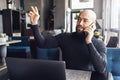 Bearded man sits in cafe at table in front of laptop, talking on phone and asking for waiter.Guy sits in restaurant,calls friends Royalty Free Stock Photo