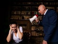 Bald boss shouting at businesswoman through loudspeaker at desk in office. Businessman with megaphone screaming at frightened Royalty Free Stock Photo