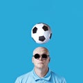 Bald brutal man in dark round glasses with highlights. A football hovered overhead. On a blue background Royalty Free Stock Photo