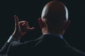 Bald business man in dark classic suit making hand gesture. Black background. Call me sign Royalty Free Stock Photo