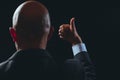Bald business man in dark classic suit making hand gesture. Black background. Thumbs ups. Good job symbol Royalty Free Stock Photo