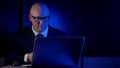 Bald businessman, in a suit and glasses, middle-aged, sitting in the dark behind a laptop, much surprised and frightened Royalty Free Stock Photo