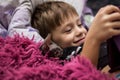 A little boy with a bald cat Sphinx lie in bed under a red blanket and look at the tablet Royalty Free Stock Photo