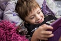 A little boy with a bald cat Sphinx lie in bed under a red blanket and look at the tablet Royalty Free Stock Photo