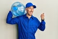 Bald courier man with beard holding a gallon bottle of water for delivery pointing thumb up to the side smiling happy with open Royalty Free Stock Photo