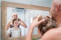 Bald dad and his long-haired teenager son in bathroom in front of the mirror. Father rising up kid`s hairs thinking about his new Royalty Free Stock Photo