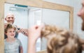 Bald dad and his long-haired teenager son in bathroom in front of the mirror. Father trying to trim long hairs showing to boy his Royalty Free Stock Photo