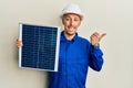 Bald engineer man with beard holding photovoltaic solar panel pointing thumb up to the side smiling happy with open mouth Royalty Free Stock Photo