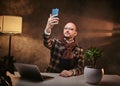 Bald european confident businessman in the office at a table with notebook, looking at smartphone, wearing stylish Royalty Free Stock Photo