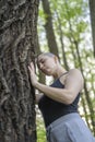 A bald girl meditates standing by a tree