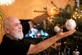 Bald and joyful elder man Decorating Christmas Tree at Home. Senior Putting up Christmas Decorations during New Year at