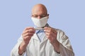 Bald male doctor looking at thermometer. Man wearing mask and glasses, light blue background. White uniform and blue shirt Royalty Free Stock Photo