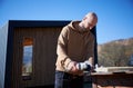 Bald male worker cutting metal, using circular saw while building wooden frame house. Royalty Free Stock Photo