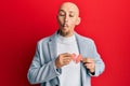 Bald man with beard holding broken heart paper shape making fish face with mouth and squinting eyes, crazy and comical Royalty Free Stock Photo