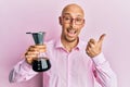 Bald man with beard holding coffee maker with filter pointing thumb up to the side smiling happy with open mouth Royalty Free Stock Photo