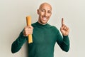 Bald man with beard holding dry spaghetti smiling with an idea or question pointing finger with happy face, number one