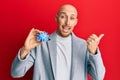 Bald man with beard holding virus toy pointing thumb up to the side smiling happy with open mouth Royalty Free Stock Photo