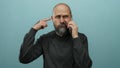 Bald man with beard talking on phone making gestures against blue background, showcasing confusion and frustration while Royalty Free Stock Photo
