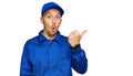 Bald man with beard wearing builder jumpsuit uniform surprised pointing with hand finger to the side, open mouth amazed expression Royalty Free Stock Photo