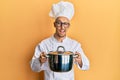 Bald man with beard wearing professional cook holding cooking pot winking looking at the camera with sexy expression, cheerful and