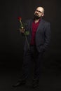 A bald man in glasses and with a beard in a suit with a red rose in his hand. Black background. Royalty Free Stock Photo