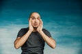 A bald man in a gray T-shirt screams, opening his eyes wide and raising his hands to his mouth like a shout. Royalty Free Stock Photo