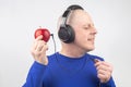 Bald man with headphones listens to music through a red apple player. Metaphor and concept of vitamin benefits in music and sound Royalty Free Stock Photo