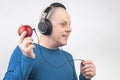 Bald man with headphones listens to music through a red apple player. Metaphor and concept of vitamin benefits in music and sound Royalty Free Stock Photo