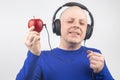 Bald man with headphones listens to music through a red apple player. Metaphor and concept of vitamin benefits in music and sound Royalty Free Stock Photo