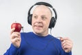 Bald man with headphones listens to music through a red apple player. Metaphor and concept of vitamin benefits in music and sound Royalty Free Stock Photo