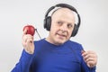 Bald man with headphones listens to music through a red apple player. Metaphor and concept of vitamin benefits in music and sound Royalty Free Stock Photo