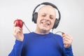 Bald man with headphones listens to music through a red apple player. Metaphor and concept of vitamin benefits in music and sound Royalty Free Stock Photo