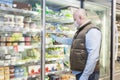 A bald man in a medical mask and gloves chooses frozen foods in a supermarket refrigerator. Proper nutrition and a healthy