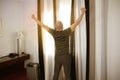 Bald man, old, stands in front of a sunny window in a hotel, arms outstretched, a suitcase on the side, business trip concept