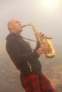 A bald man plays on a gold alto saxophone in the nature, against Royalty Free Stock Photo